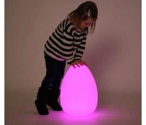 child playing with a large sensory mood egg lit up in pink in a darkened room