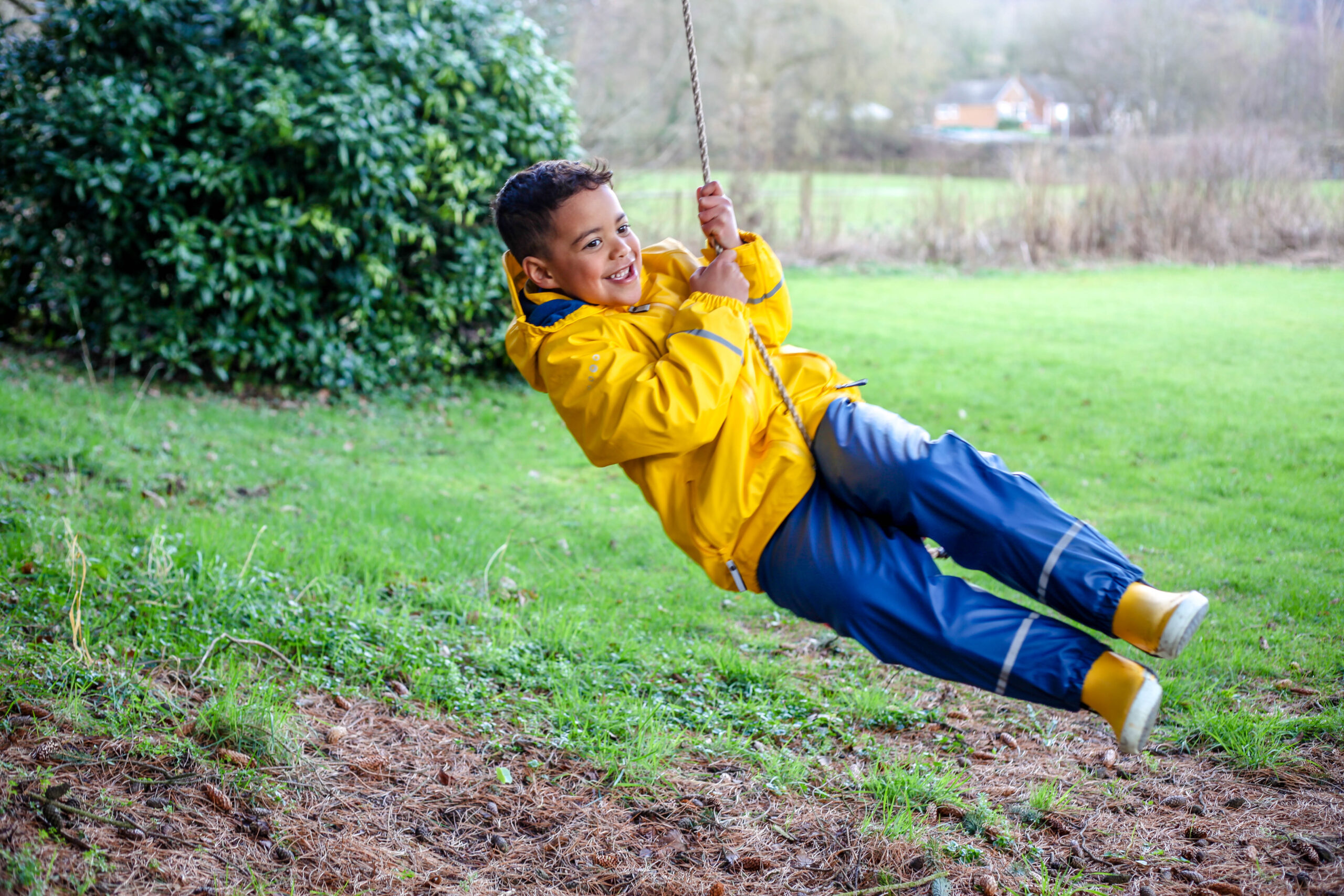 Child on rope swing wearing Spotty Otter Forest Leader jacket and dungarees