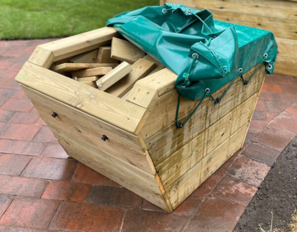Outdoor wooden skip and blocks for early years construction with PVC green cover pulled back to reveal blocks in the skip.