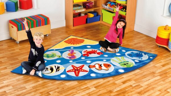 Corner classroom carpet featuring images of sea creatures. Two children sat on carpet raising hands to answer questions