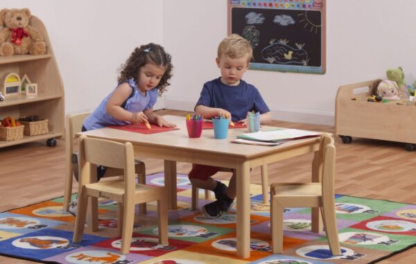 Two children sitting at a rectangular wooden classroom table in a classroom setting