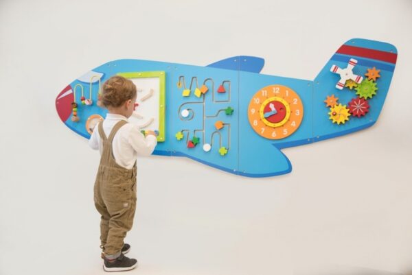Child playing with wall mounted Aeroplane Activity Panel Set. Aeroplane has various puzzles for young children including wire bead frame, clock, shape maze and gears and cogs