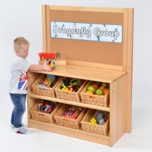 Child stood in front of a Room Scene Angled Classroom Tidy with Cork Board with 6 wicker baskets containing toys and cork noticeboard on top of the shelves