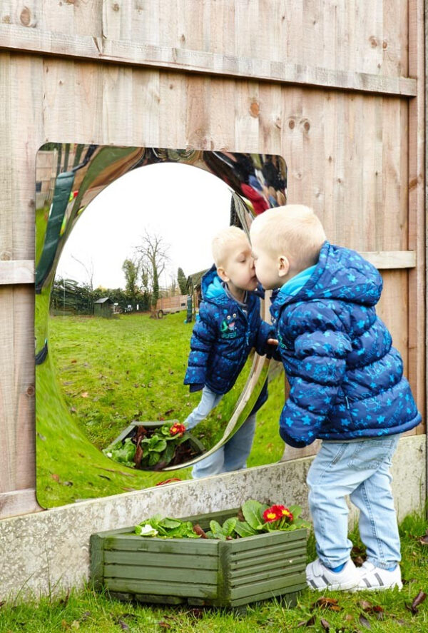 Little boy looking in a giant acrylic mirror panel with dome in centre creating distortion