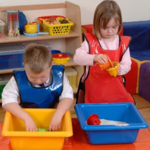Children wearing PVC tabards while engaging in messy play at a table