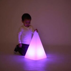 Child looking at a sensory mood pyramid light illuminated in a darkened room