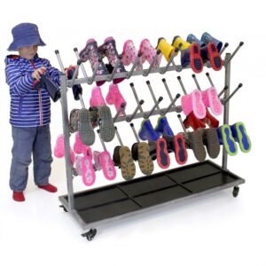 Primary boy placing his wellies on metal welly rack on wheels. The rack holds 30 pairs of wellies and has three rows on each sides with posts for each boot