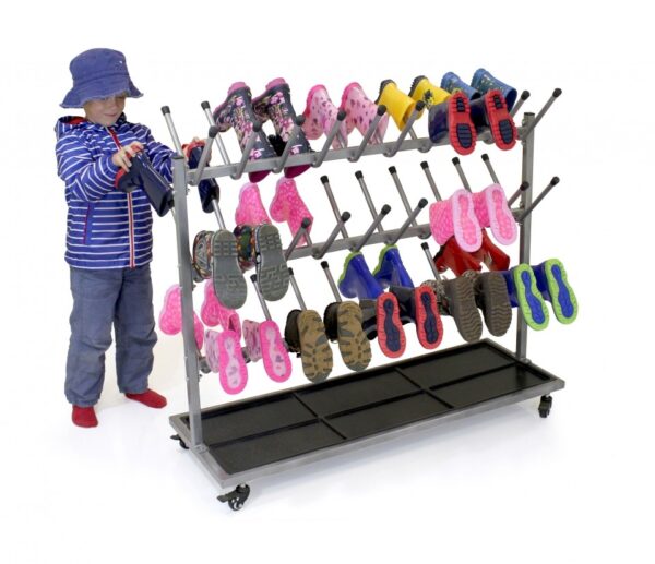 Primary boy placing his wellies on metal welly rack on wheels. The rack holds 30 pairs of wellies and has three rows on each sides with posts for each boot