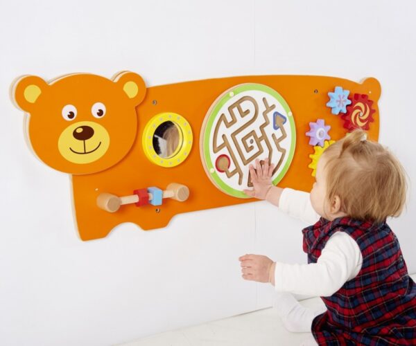 Child playing with orange wall mounted bear game containing various puzzles for children