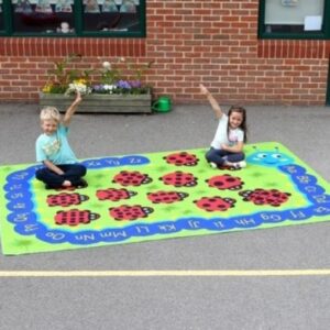 3 x 2m outdoor play mat with graphics of a caterpillar with the alphabet on its back and in the centre of the mat ladybirds with different number of spots on each one. Two children are sat on the mat in a playground raising their hands to answer a question