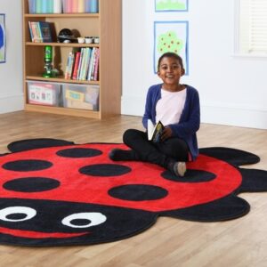 Giant classroom rug shaped like a ladybird with child sat smiling and holding a book
