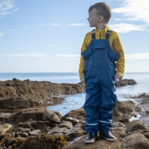 Little boy wearing Spotty Otter Forest Leader Dungarees on a beach